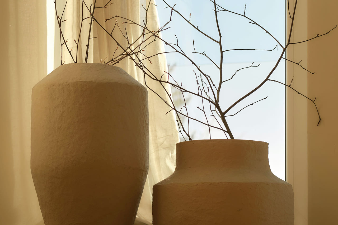Two textured clay vases holding bare branches in soft window light.