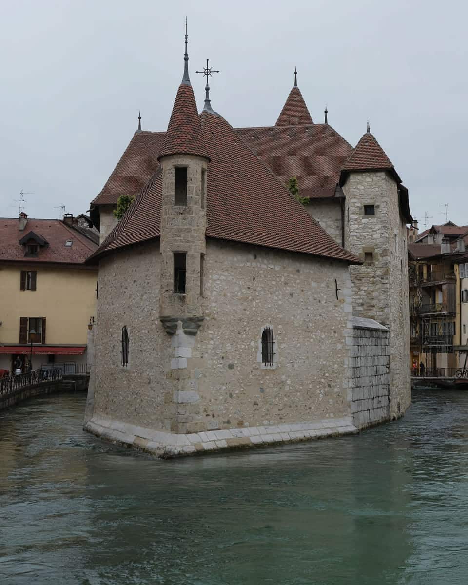 The Palais de l’Isle seen from the side: a stone house with a pointed tiled roof and a small turret, rising straight from the canal.
