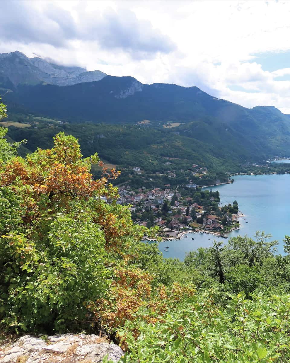 The view from the Roc de Chère: wooded rocks and autumn foliage above the lake, with mountains across the water.