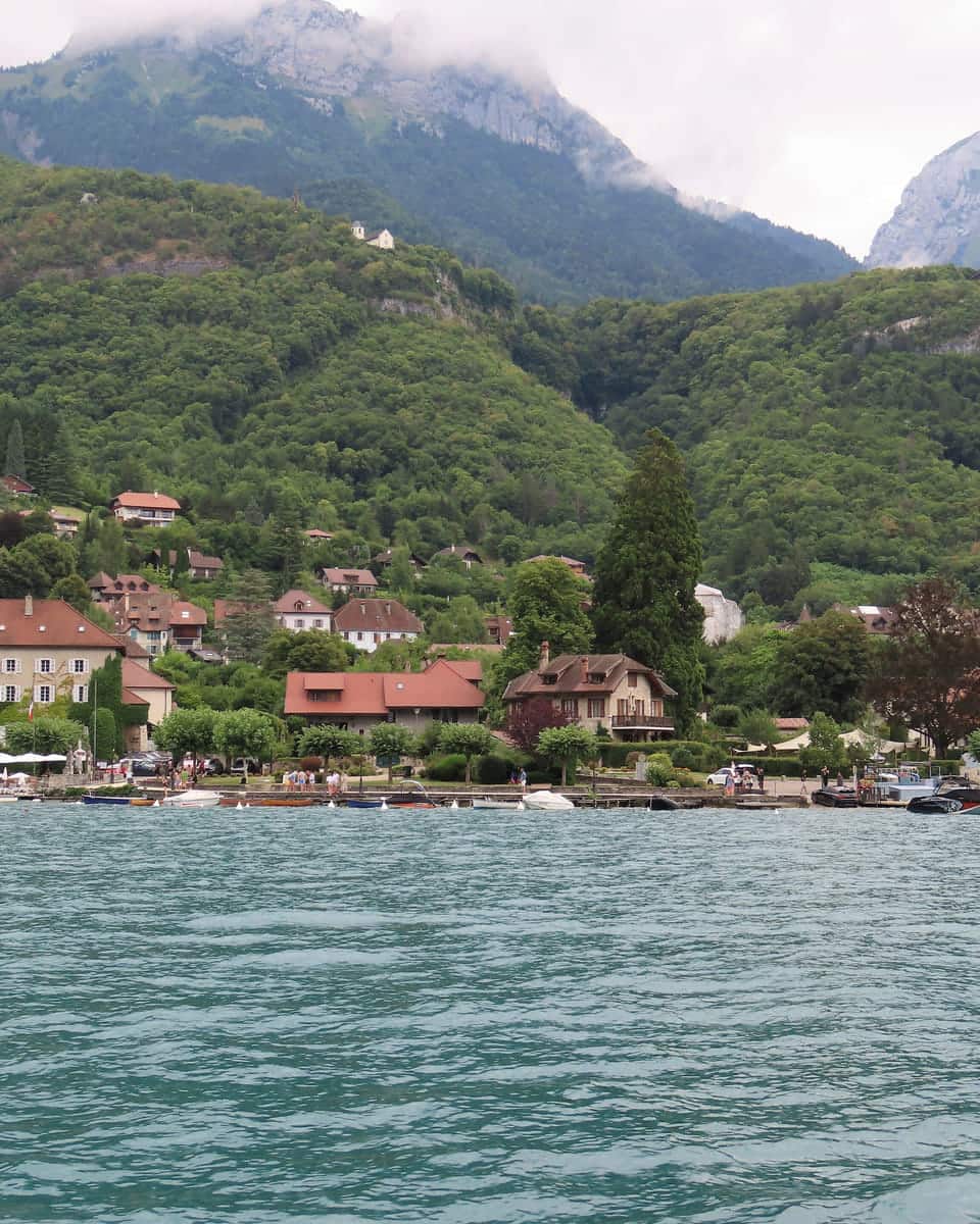 Talloires seen from the water: a village of pale houses under steep green mountains.