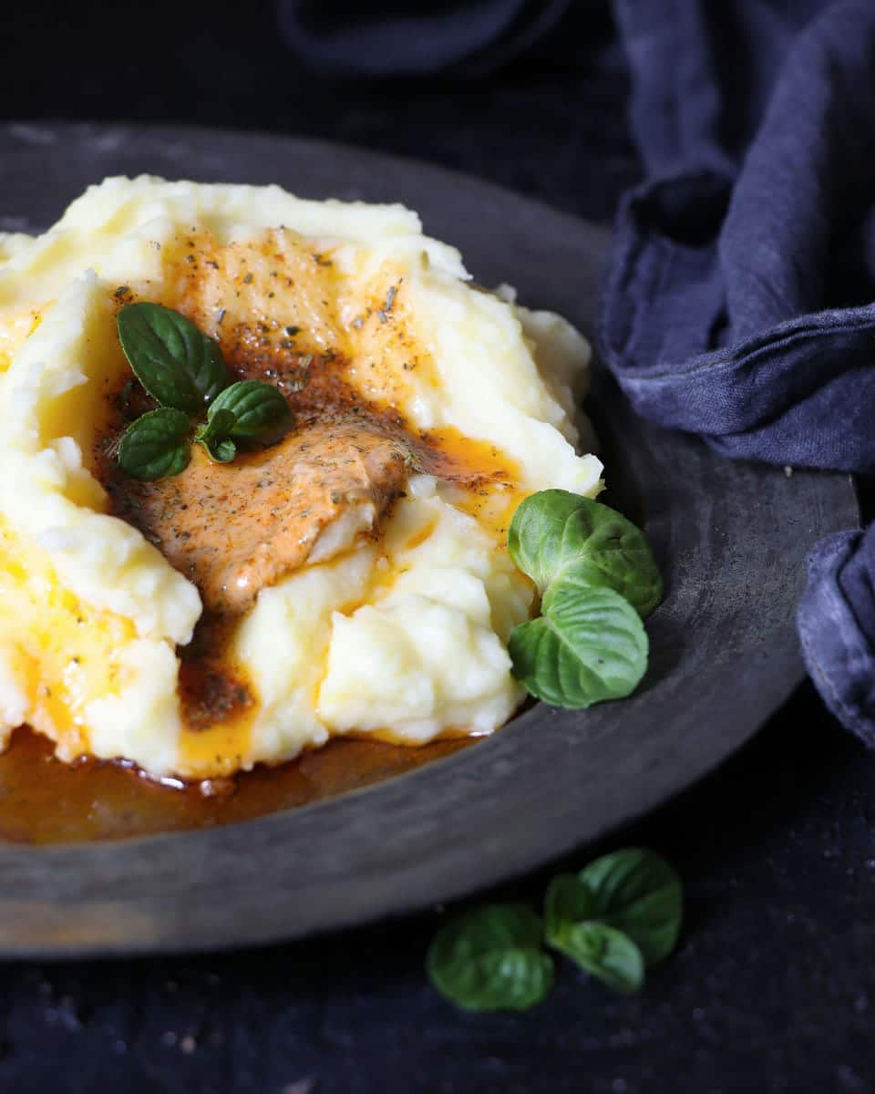 Mashed potatoes topped with brown gravy and basil leaves on a dark plate.