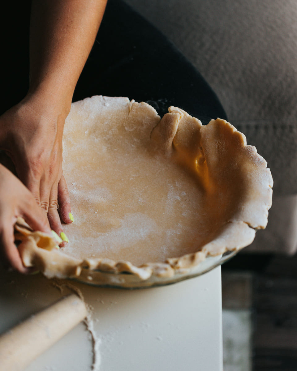 Hands crimping the edge of a pie crust in a white dish.