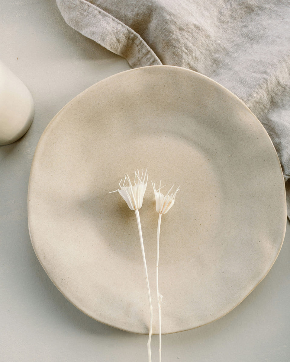 A hand-thrown cream stoneware plate with two dried white flowers.