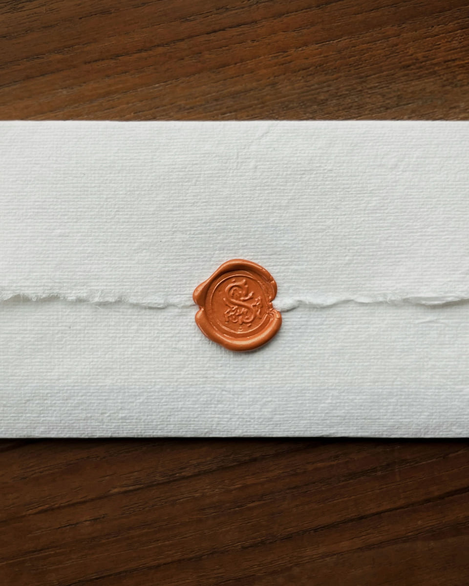 A folded sheet of handmade paper sealed with a copper wax seal, on a dark wooden table.