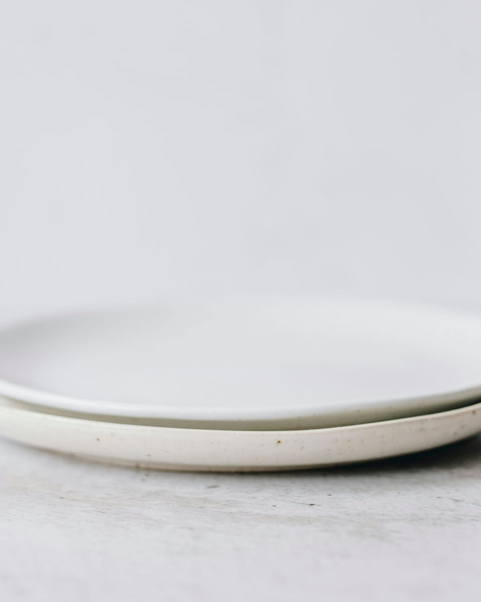 Two plain white porcelain plates stacked on a white table.